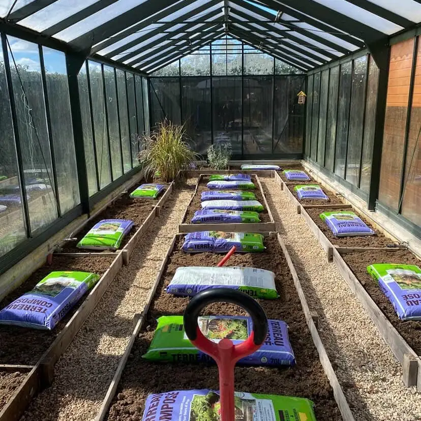 Intérieur d'une serre avec des carrés de potager préparés et des sacs de terreau, à Bras